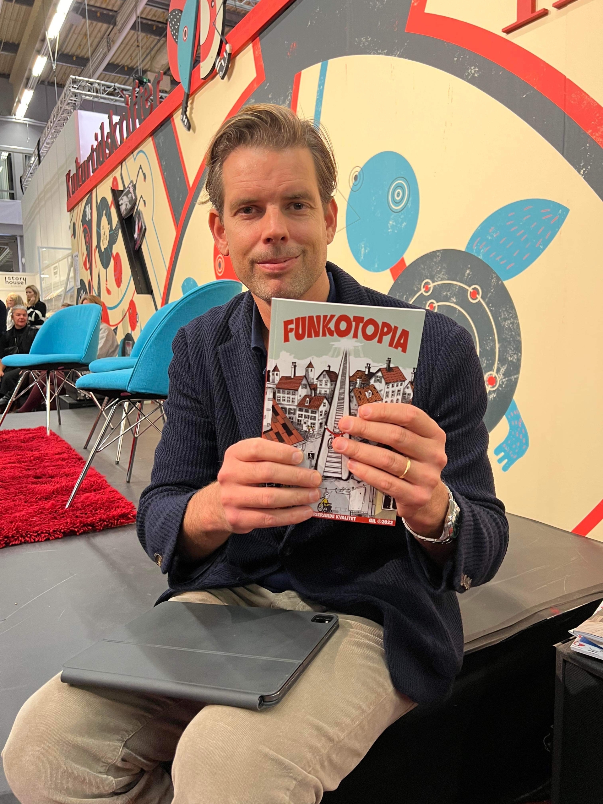 Foto av Alex Schulman som håller upp boken Funkotopia